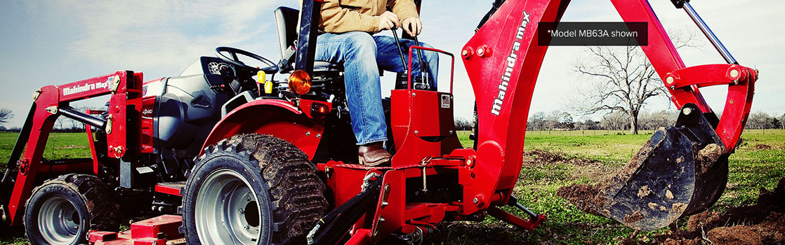 An individual operating a Mahindra® backhoe and digging up dirt in a field.